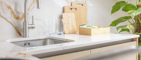 A kitchen with a modern faucet, marble backsplash, wooden cutting boards, and a plant.