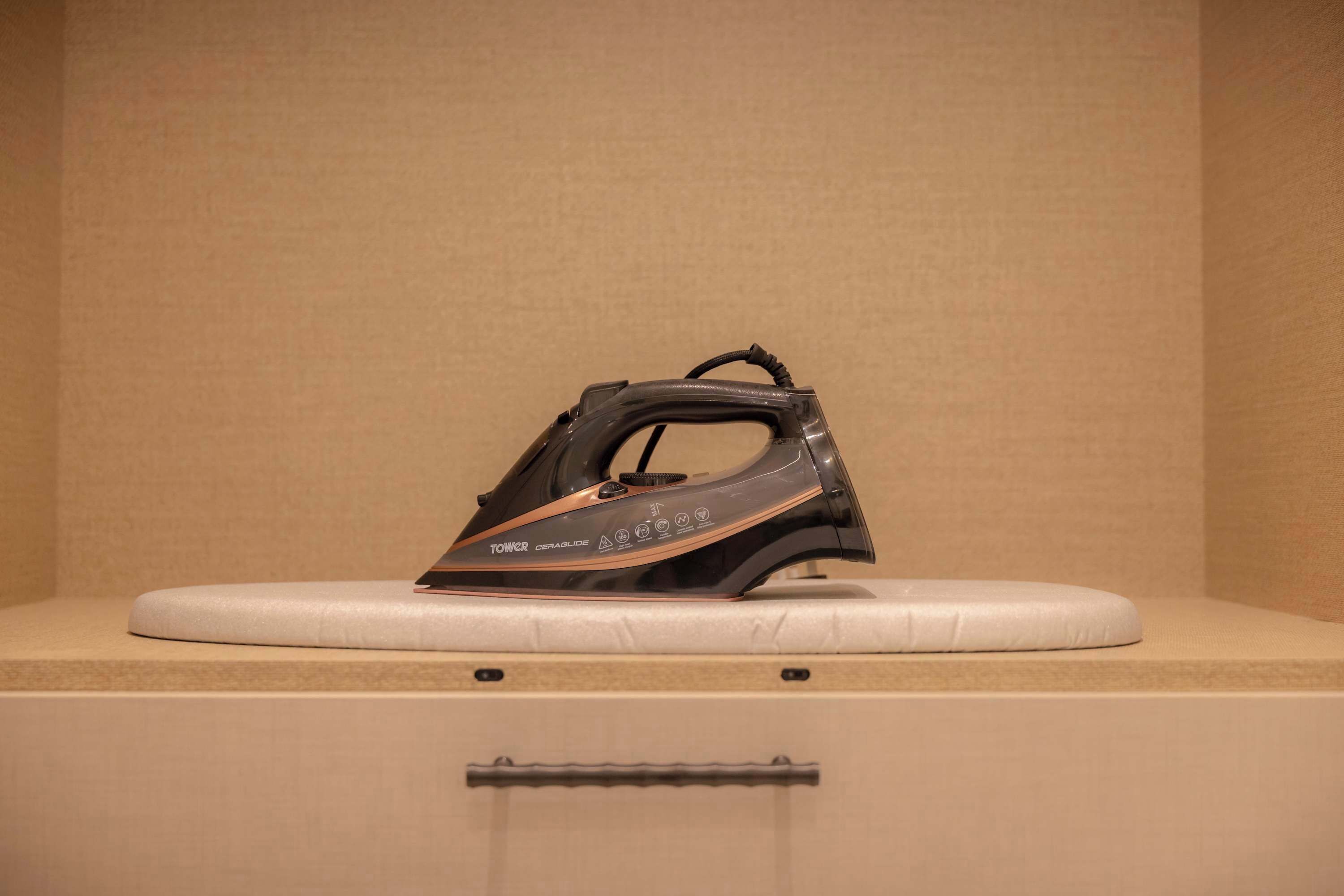 An iron on a flat surface with a beige wall in the background.