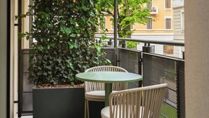 A balcony with a round table and two chairs, a large potted plant, and a view of buildings. - Limehome Milan Navigli (Milan)
