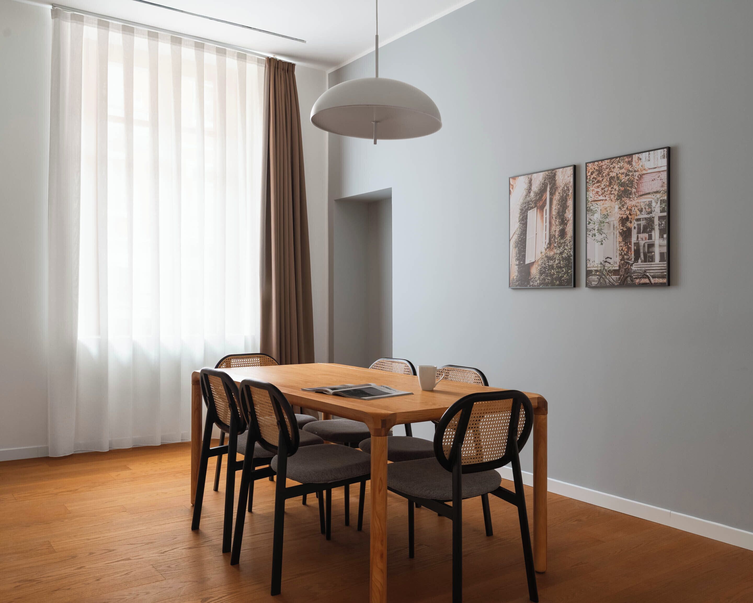 Een eetruimte met een houten tafel, zwarte stoelen, een witte hanglamp en twee ingelijste foto's aan de muur.
