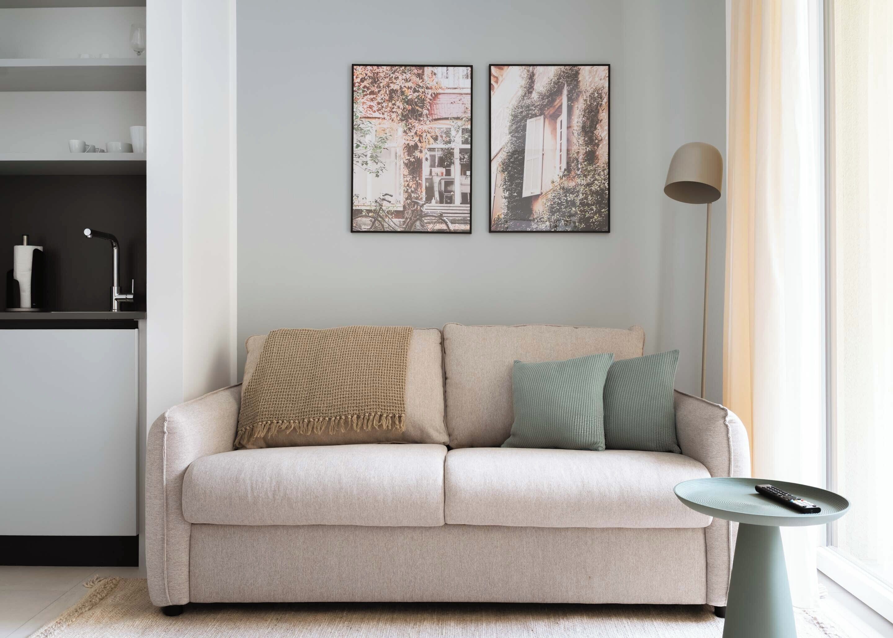 A living room with a sofa, a small table with a remote, and two framed pictures on the wall.