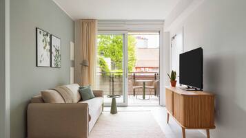 Un salon moderne avec un canapé, un téléviseur posé sur un meuble en bois, une petite table et un balcon donnant sur un paysage verdoyant.