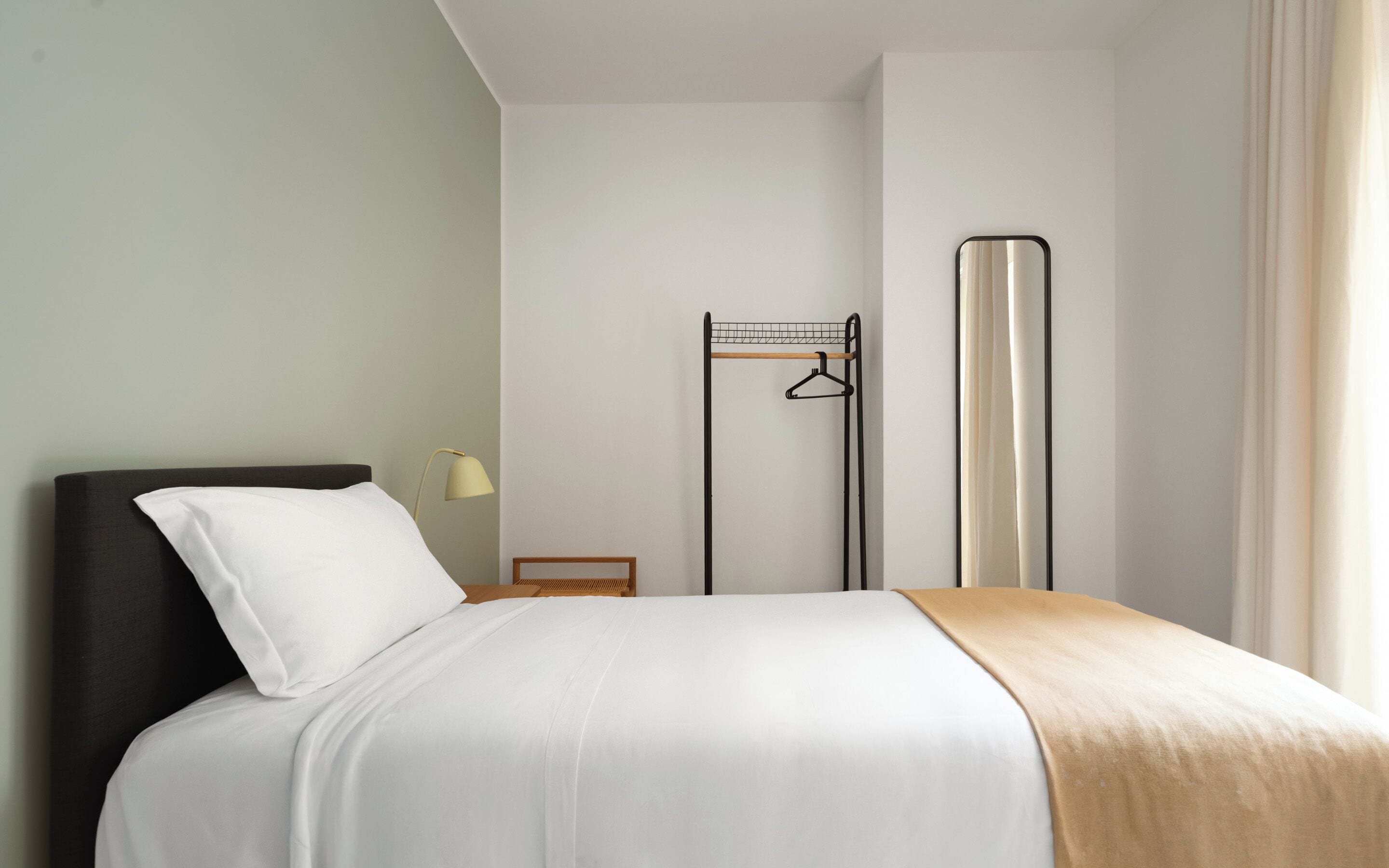 A hotel room with a bed, a bedside table with a lamp, a wardrobe, and a mirror.