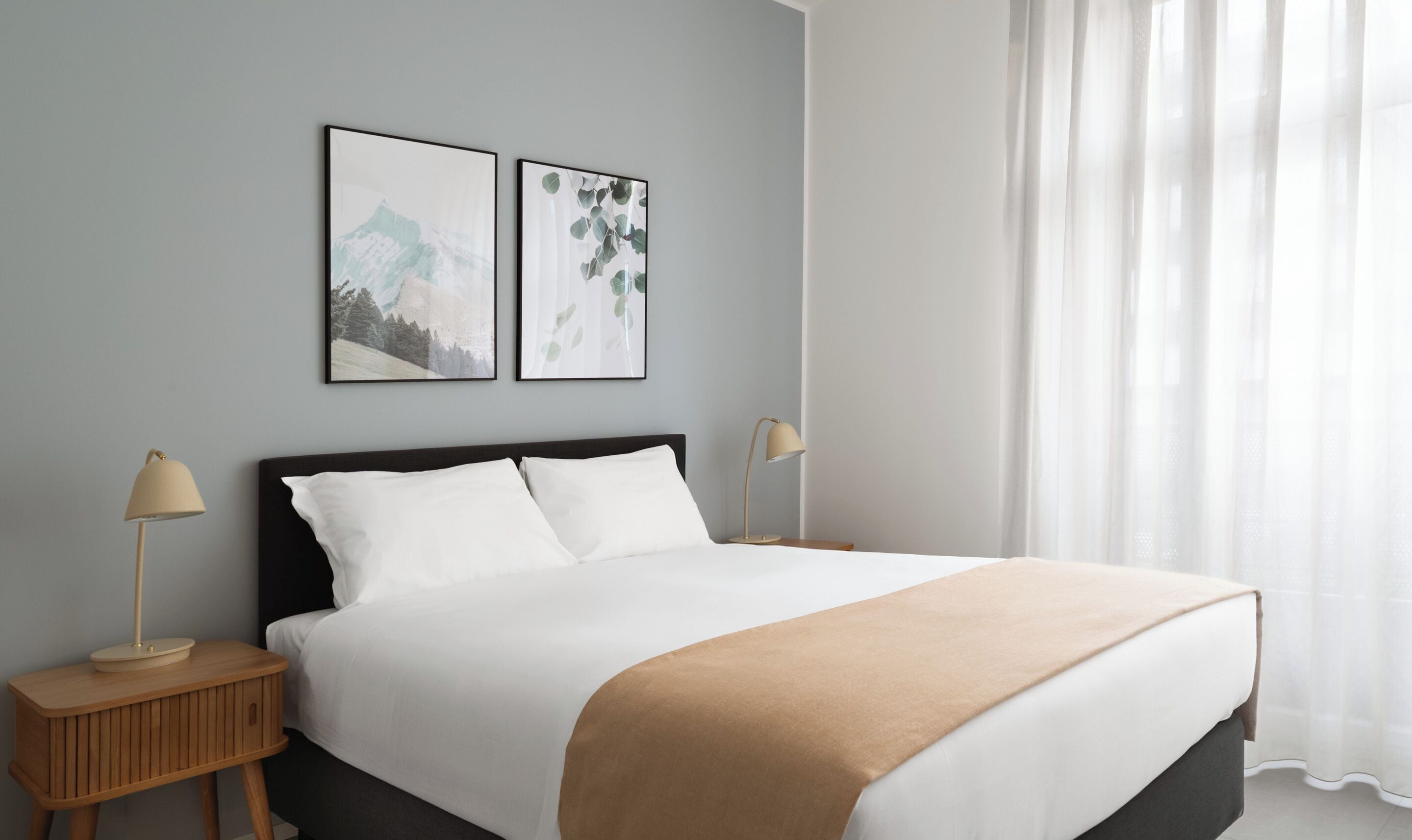 A neatly made bed with a dark headboard, two bedside tables with lamps, and two framed pictures on the wall.