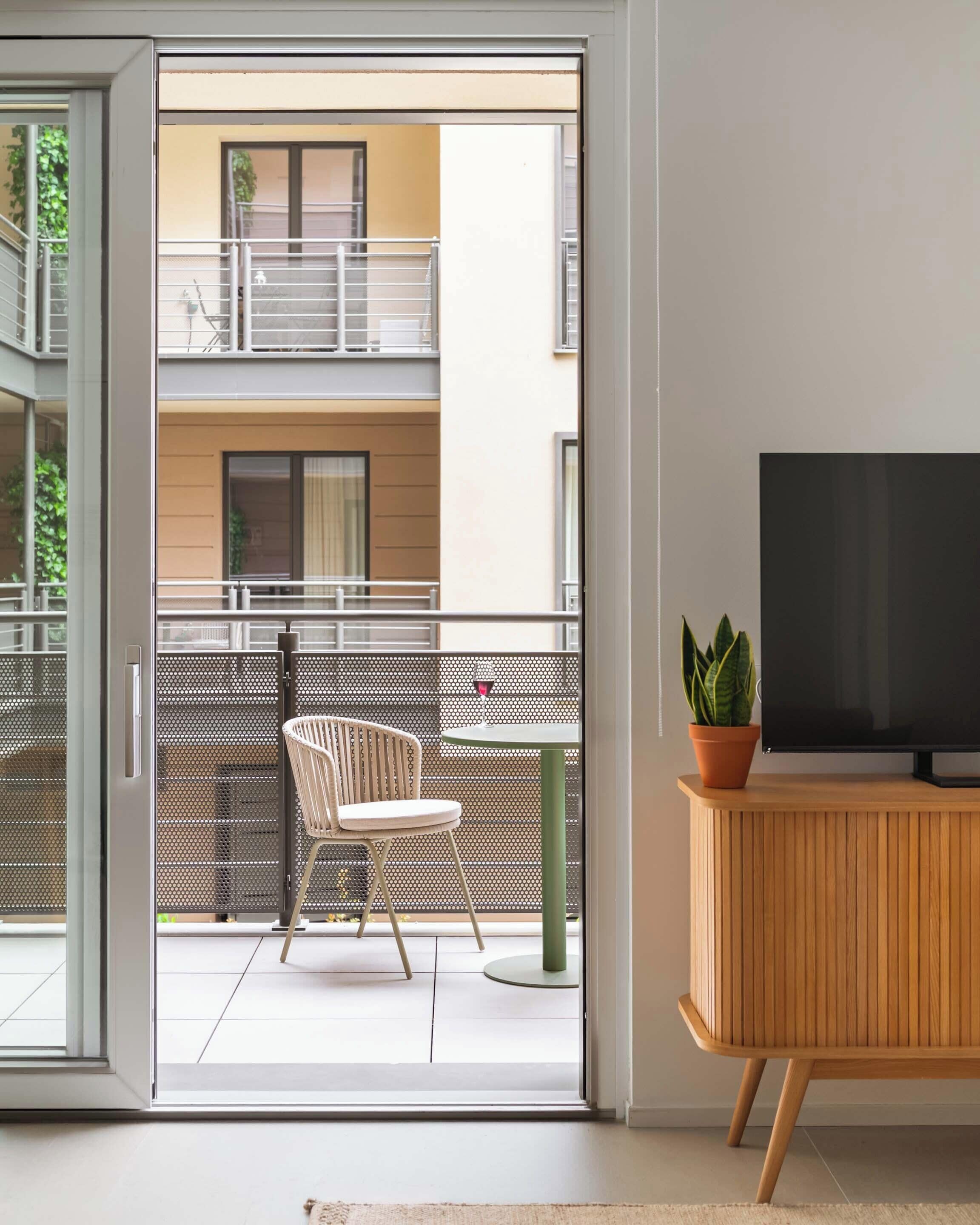 A modern living room with a sliding glass door leading to a balcony, a wooden TV stand, and a potted plant.