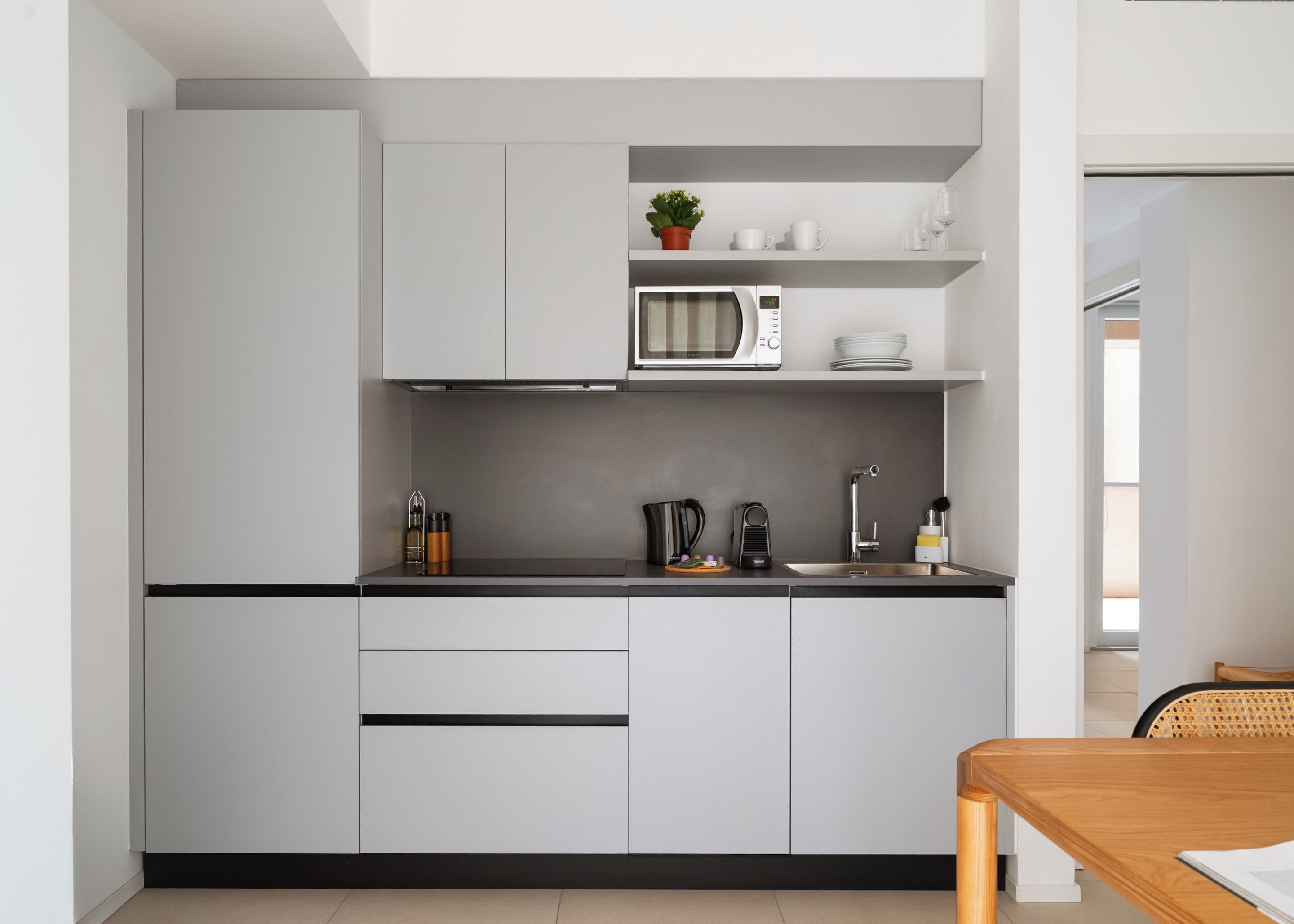 Een moderne keuken met witte kastjes, een magnetron, waterkoker en spoelbak.