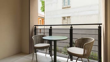 Un balcon avec deux chaises et une table, une clôture en métal et une vue sur un immeuble aux fenêtres grillagées.