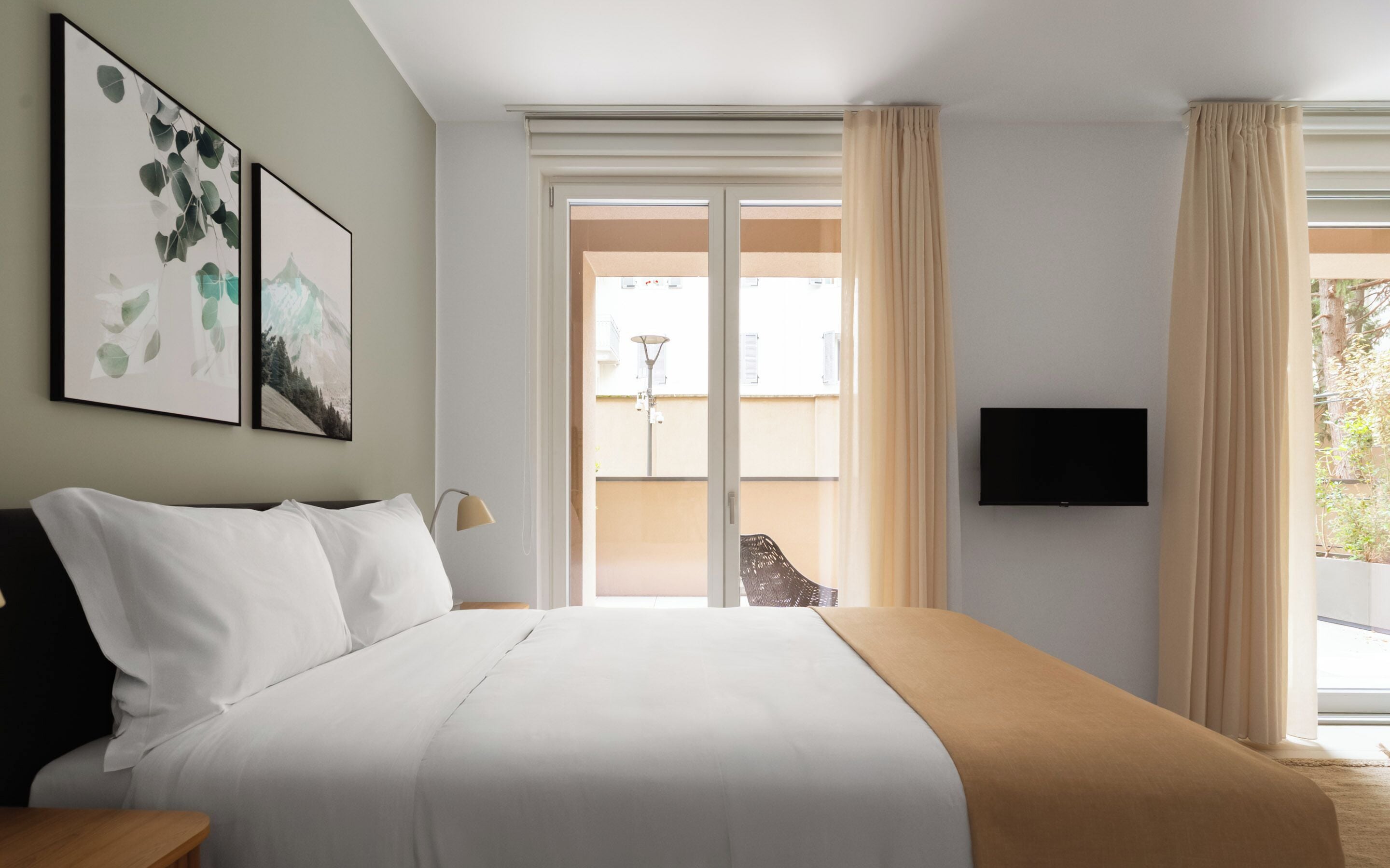 A hotel room with a bed, a TV, and a view of the outside.