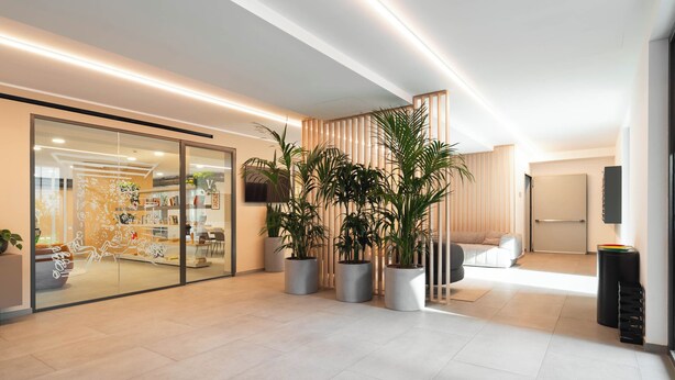 A modern interior with a glass door entrance, potted plants, a sofa, and a flat-screen TV. - Limehome Milan Navigli (Milan)