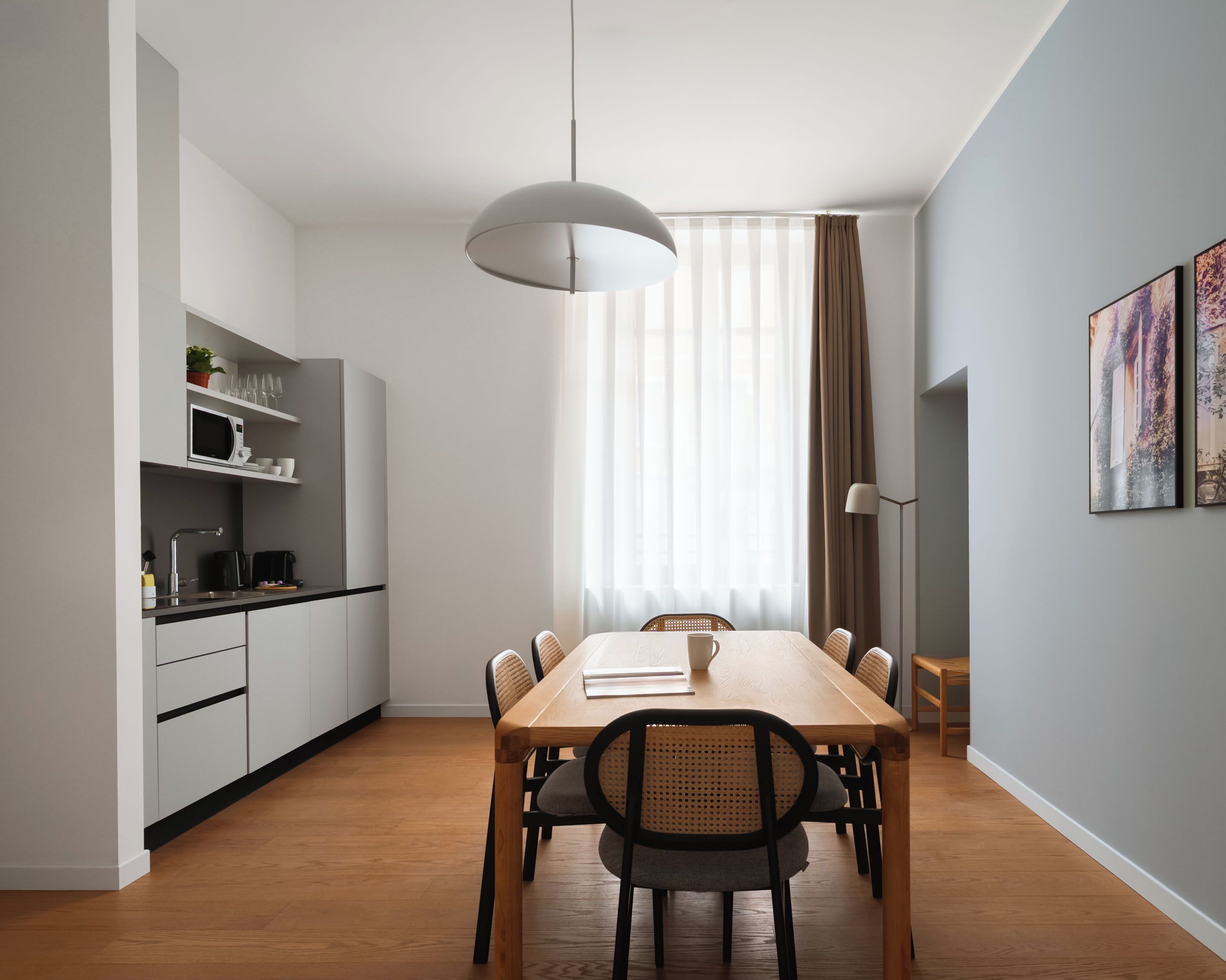 A modern kitchen with white cabinets, a wooden dining table, and a hanging light fixture.