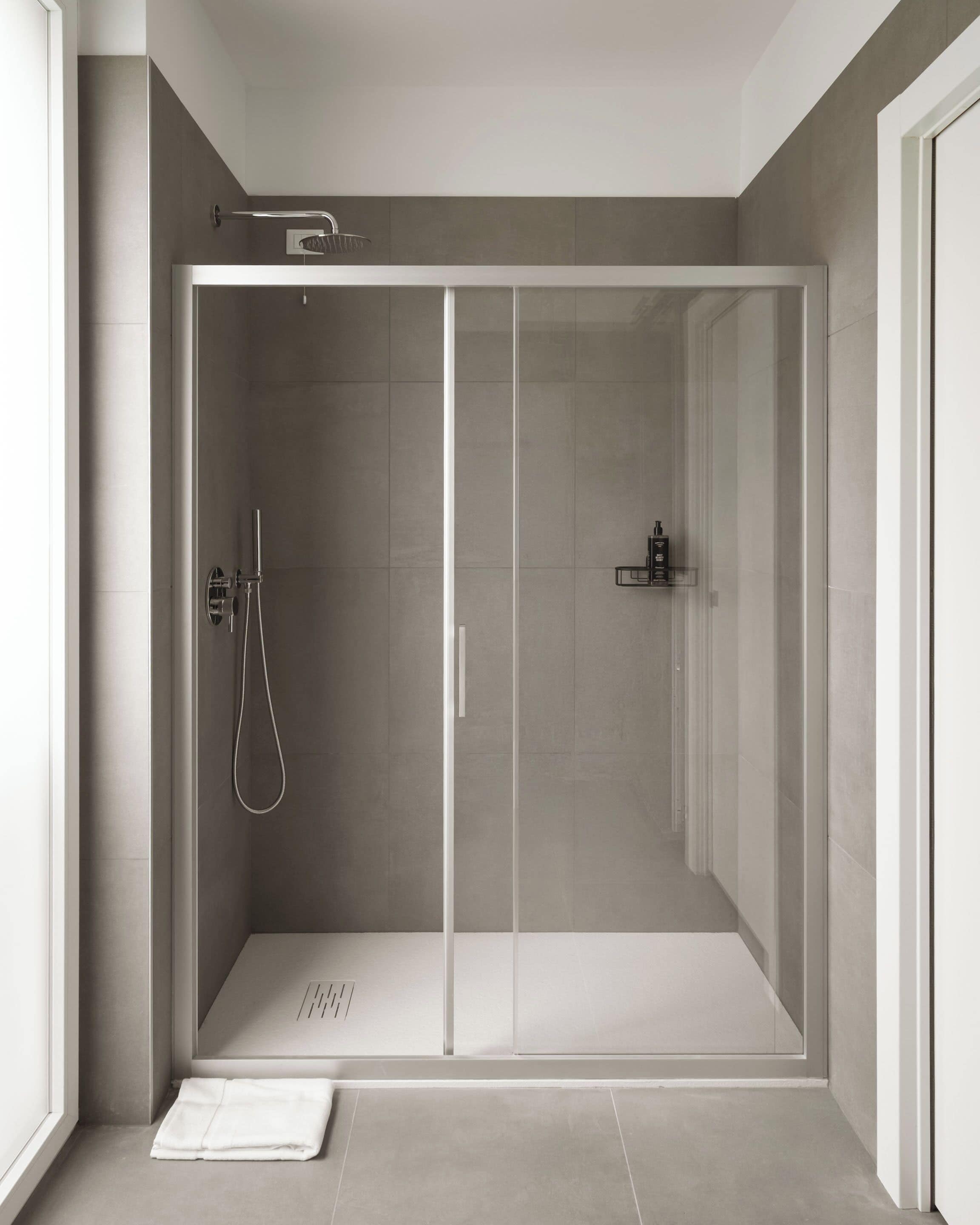 Een moderne badkamer met een glazen deur, een handdouche en een handdoek op de vloer.