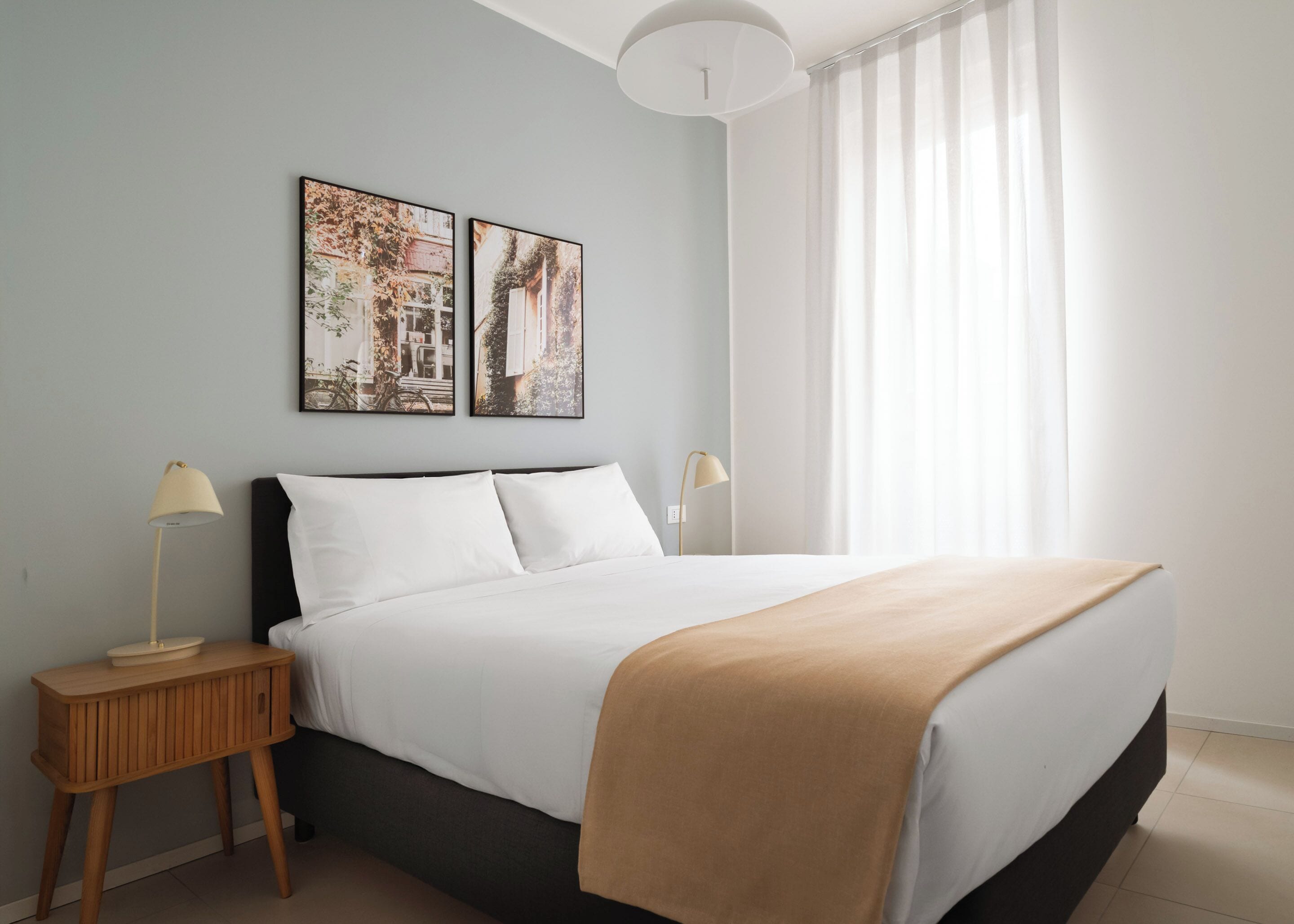 Une chambre à coucher avec un lit, deux tables de chevet, une lampe sur chaque table et deux tableaux encadrés au mur.