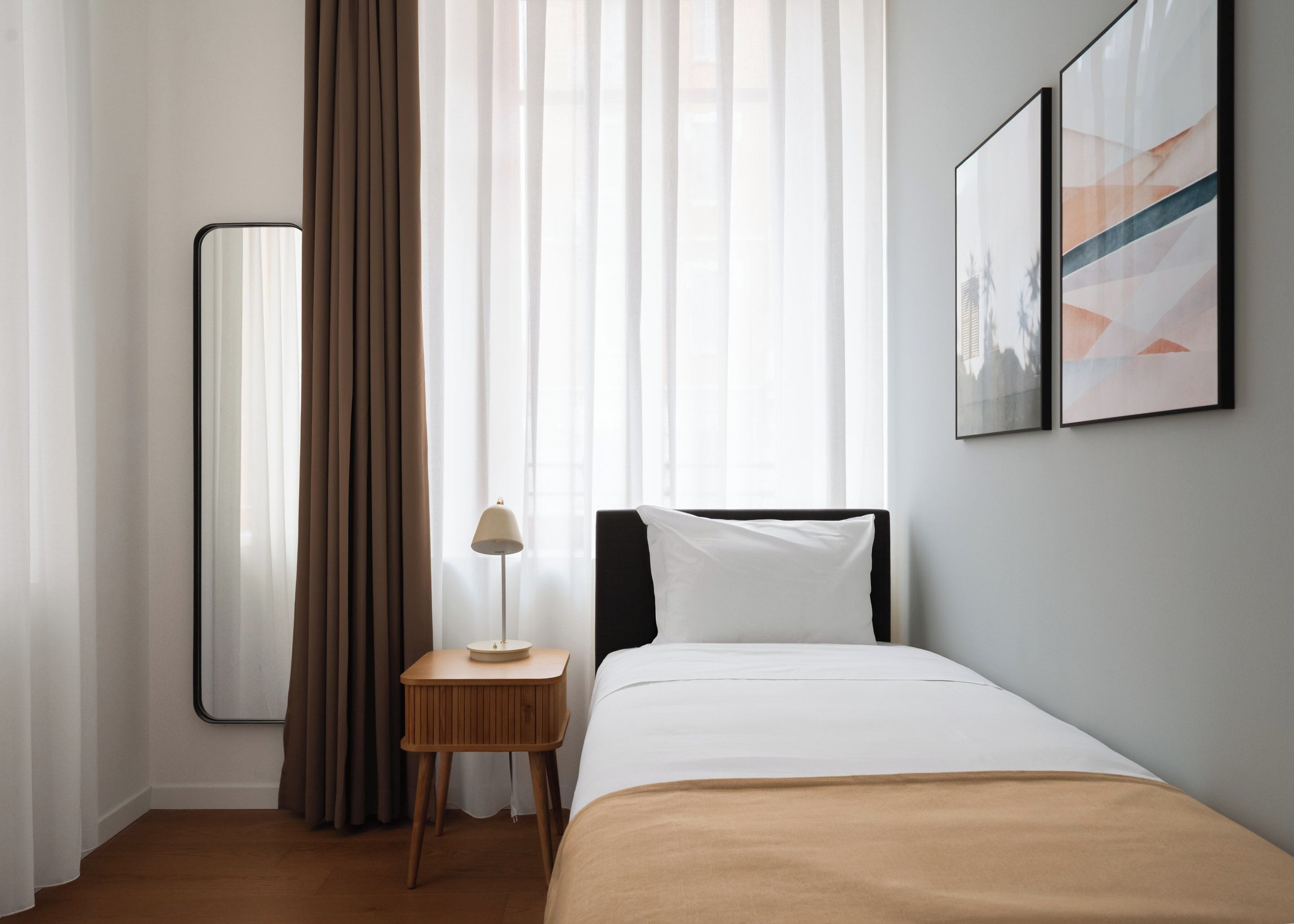 A hotel room with a bed, a bedside table with a lamp, a mirror, and abstract wall art.