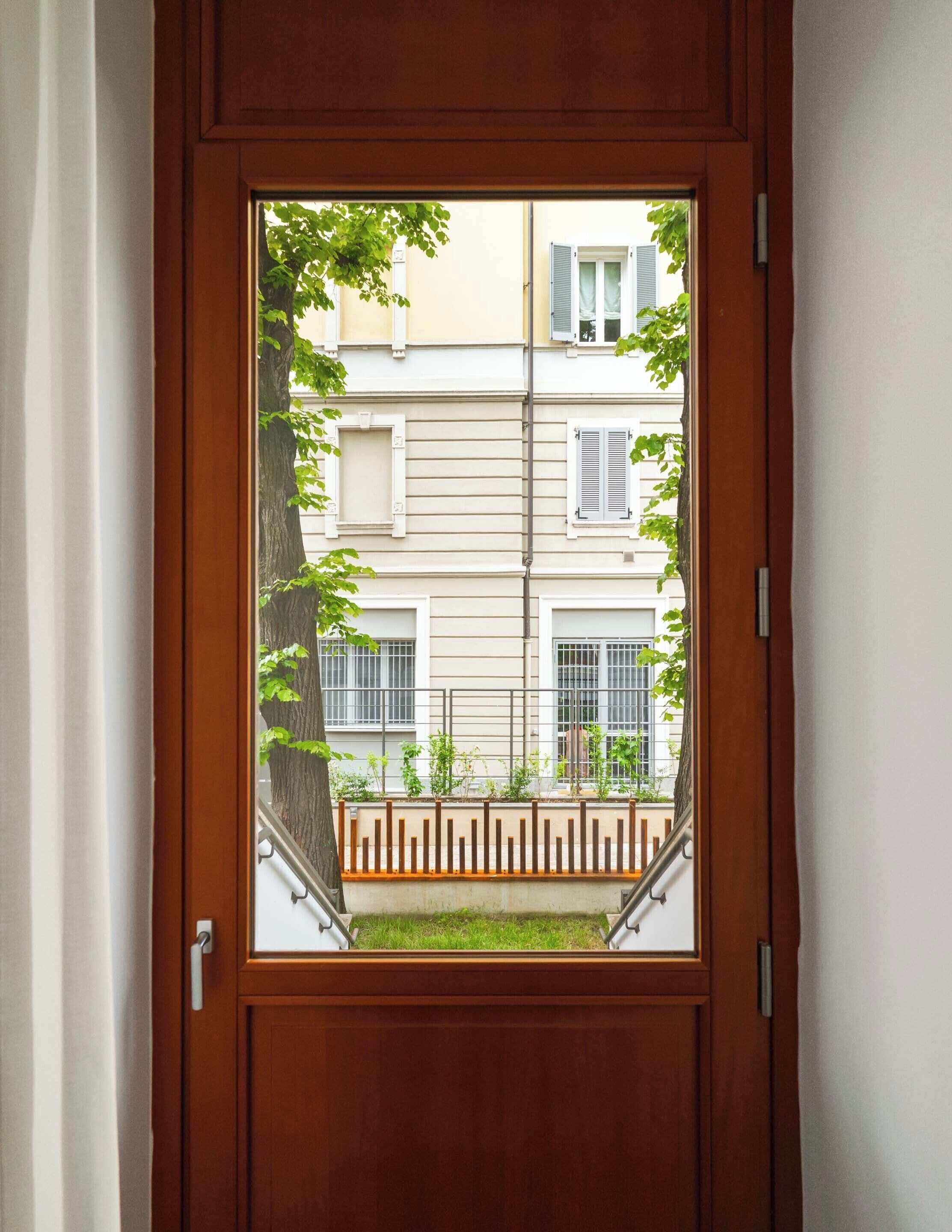 Puerta de madera que da a una vista de un edificio con ventanas con barrotes y un pequeño jardín.