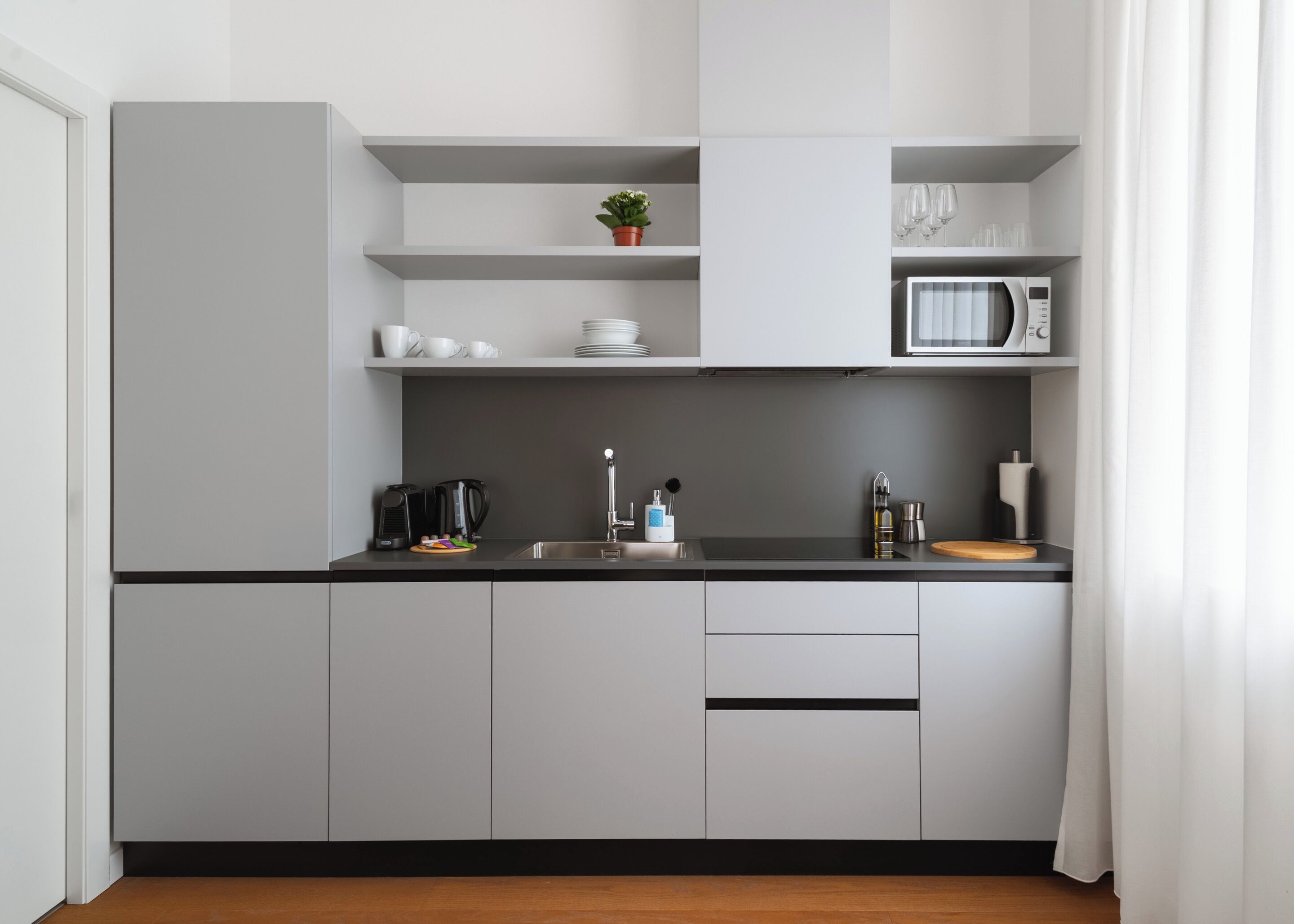 A modern kitchen with grey cabinets, a black countertop, a microwave, and a coffee maker.