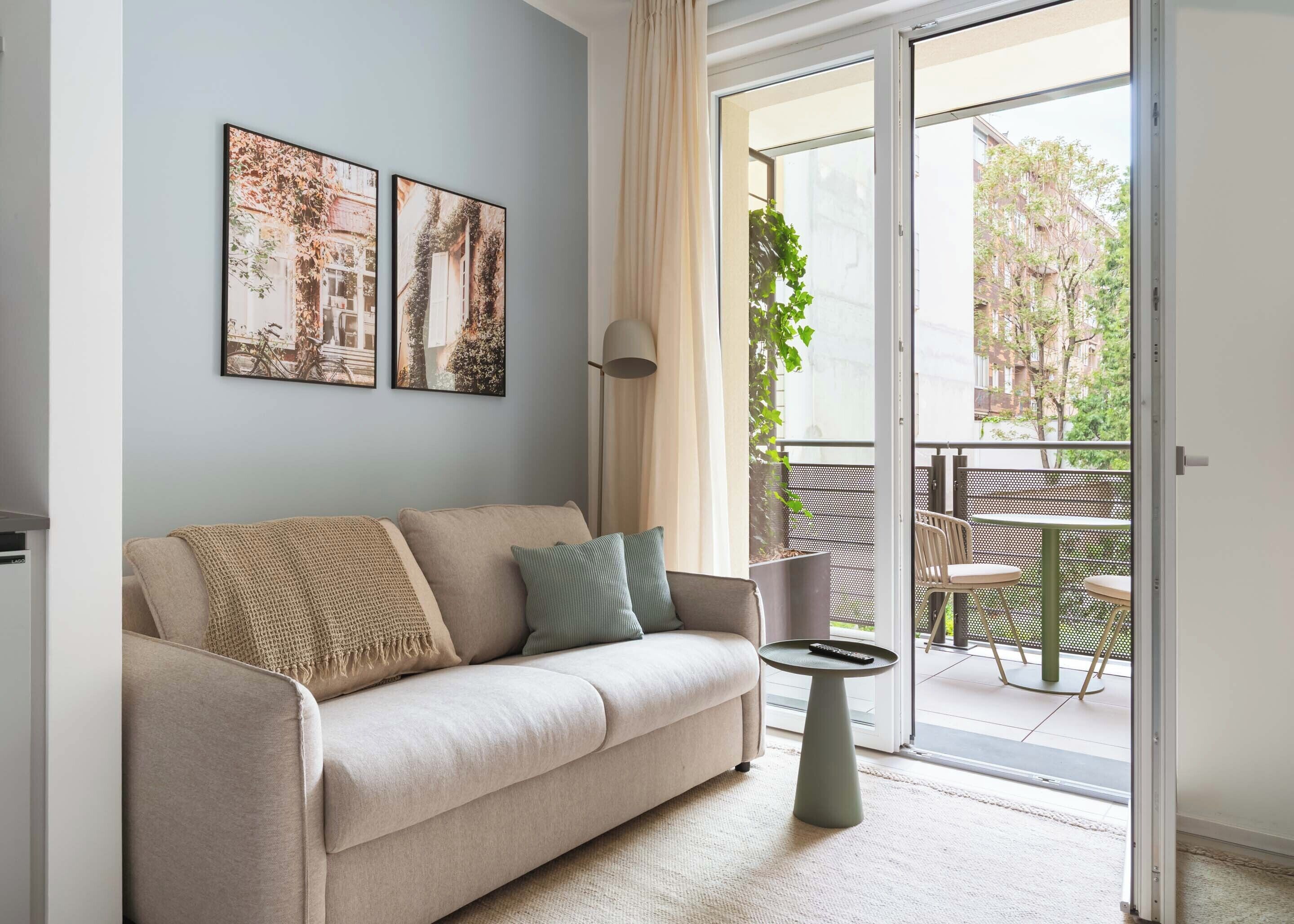 A living room with a sofa, a small table, and a balcony with outdoor furniture.