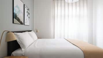 A modern hotel room with a bed, bedside tables, a lamp, and a large window with sheer curtains.