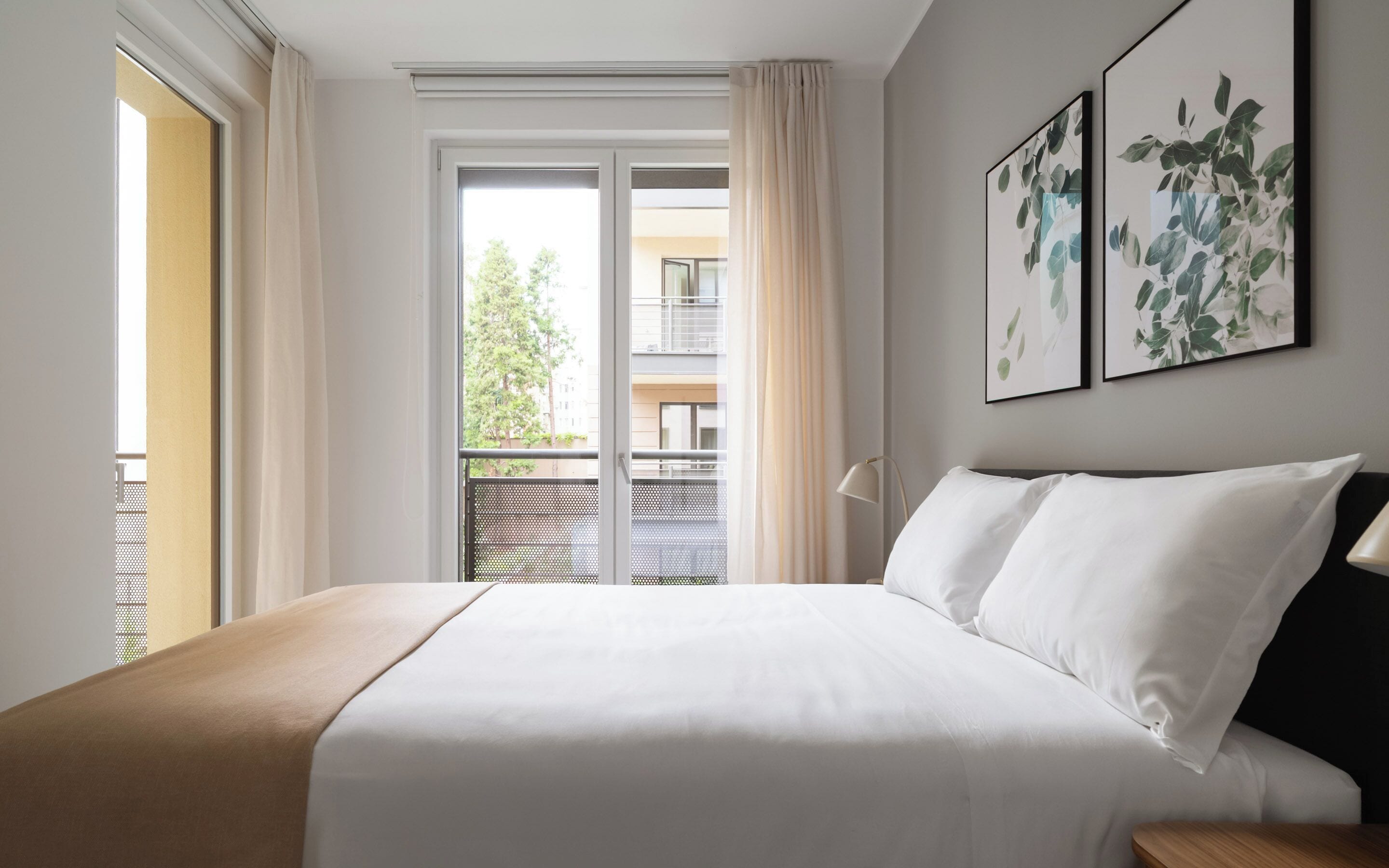 Quarto com cama, janela com cortinas e duas imagens emolduradas na parede.