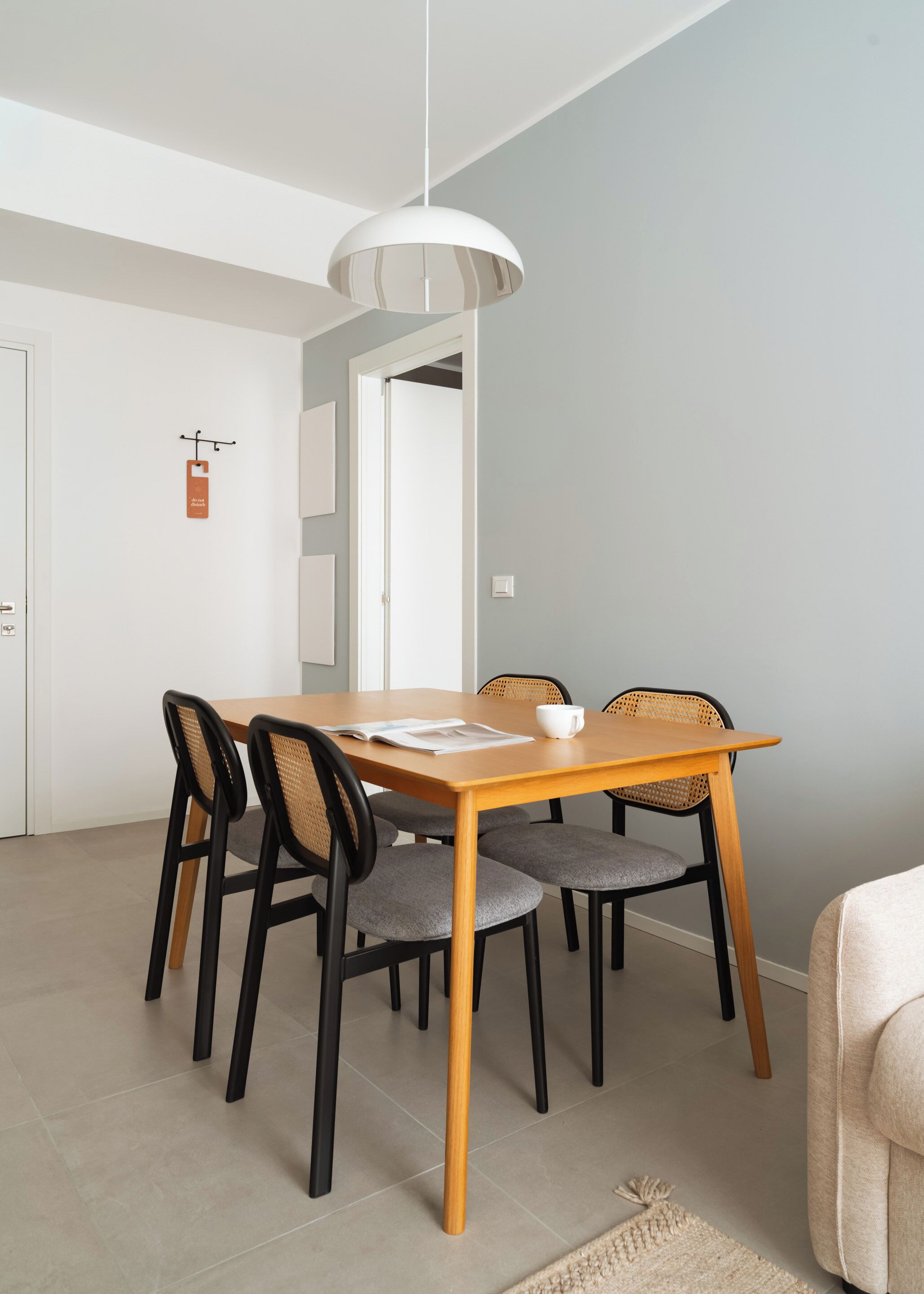 A dining area with a wooden table, six chairs, a hanging light fixture, and a door with a sign.