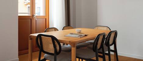 A dining area with a wooden table, six chairs, a hanging light fixture, and a window with curtains.