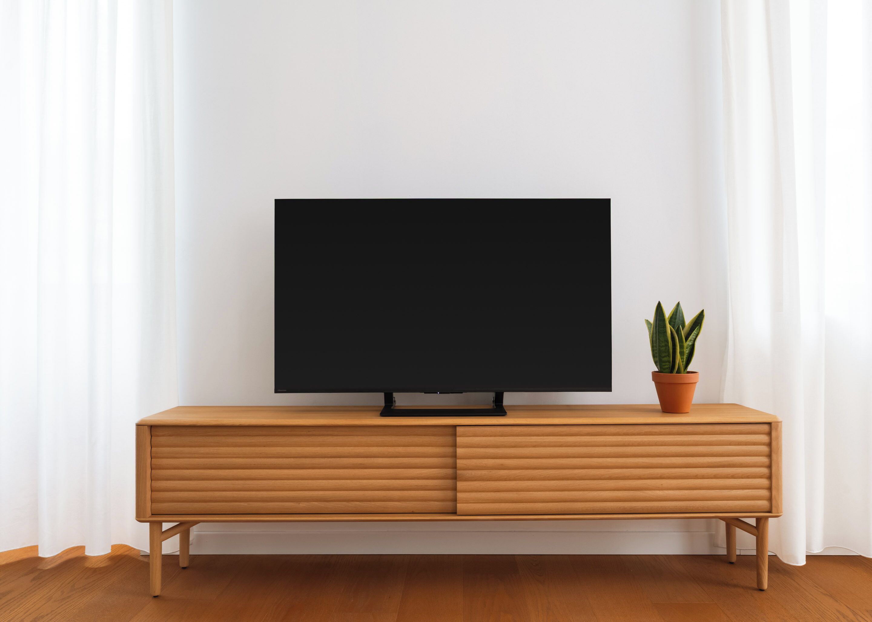 A television on a wooden cabinet with a potted plant beside it.
