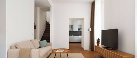 A modern living room with a sofa, coffee table, TV, and a kitchen in the background.