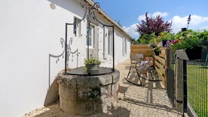 Un edificio blanco con un pozo de piedra, una valla de madera y un jardín con diversas plantas.