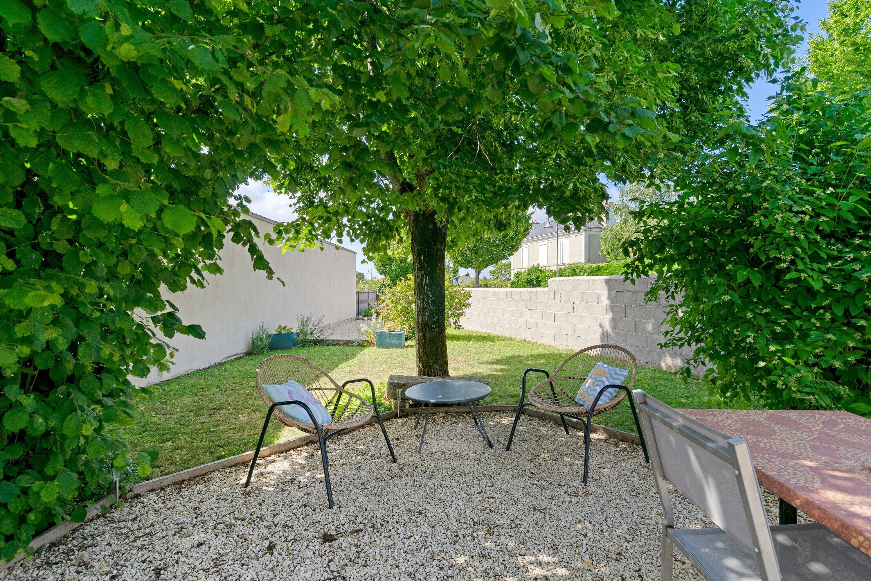 Un espace extérieur aménagé avec des chaises et une table, entouré de gravier et de verdure.