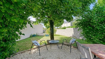 Un espace extérieur aménagé avec des chaises et une table, entouré de gravier et de verdure.