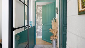 Un couloir avec une porte verte, une plante en pot et un mur orné d’une fresque.