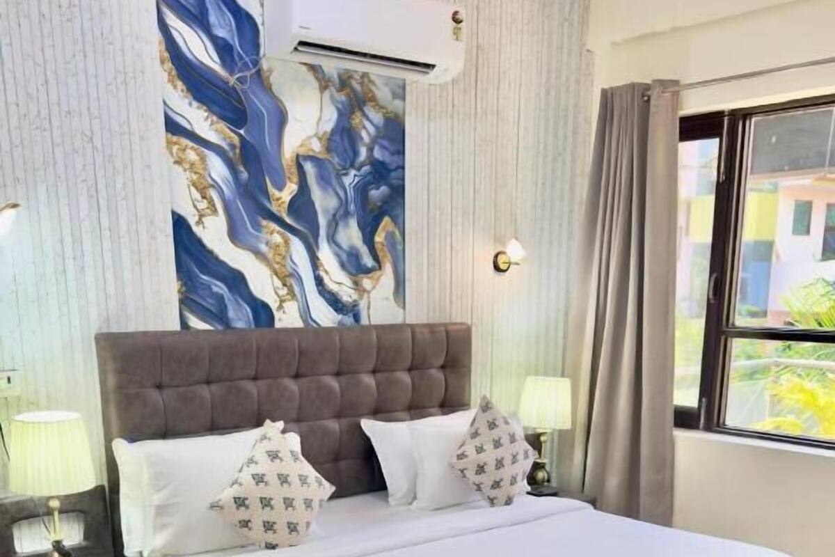 Una cama bien tendida con cabecera gris, sábanas blancas y almohadas estampadas.