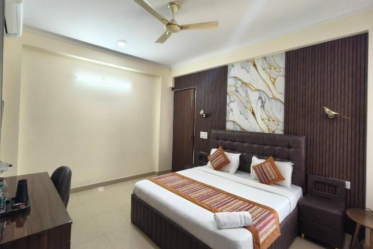 Habitación de hotel con cama, escritorio, silla, mesita y ventilador de techo.