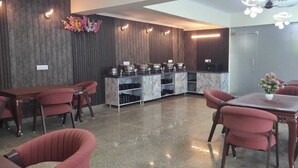 Eine Hotelhalle mit einem мраморным Empfangsschalter, roten Polstersesseln, einem Frühstücksbereich und einer Blumentopf-Pflanze.