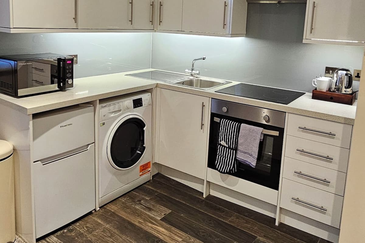 Uma cozinha compacta com armários brancos, forno embutido, micro-ondas e máquina de lavar.