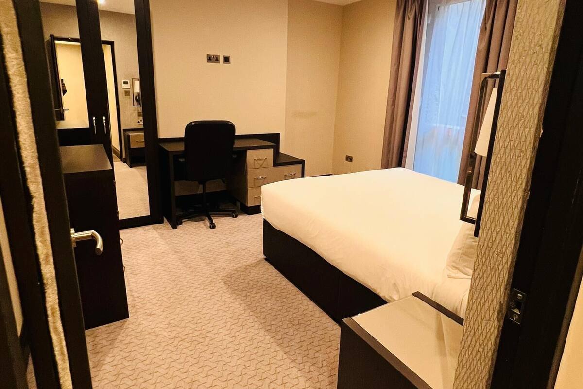 Quarto de hotel com cama, escrivaninha, cadeira e um pequeno armário.