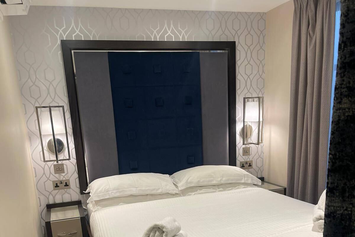 Quarto de hotel com uma cama grande, cabeceira, mesas de cabeceira com abajures e parede estampada.