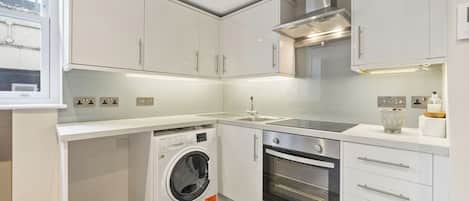 A compact kitchen with a washing machine, oven, and stainless steel cabinets.