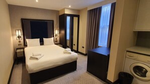 Ett hotellrum med en stor säng, sänglampor, en garderob, en tvättmaskin och ett fönster med gardiner.