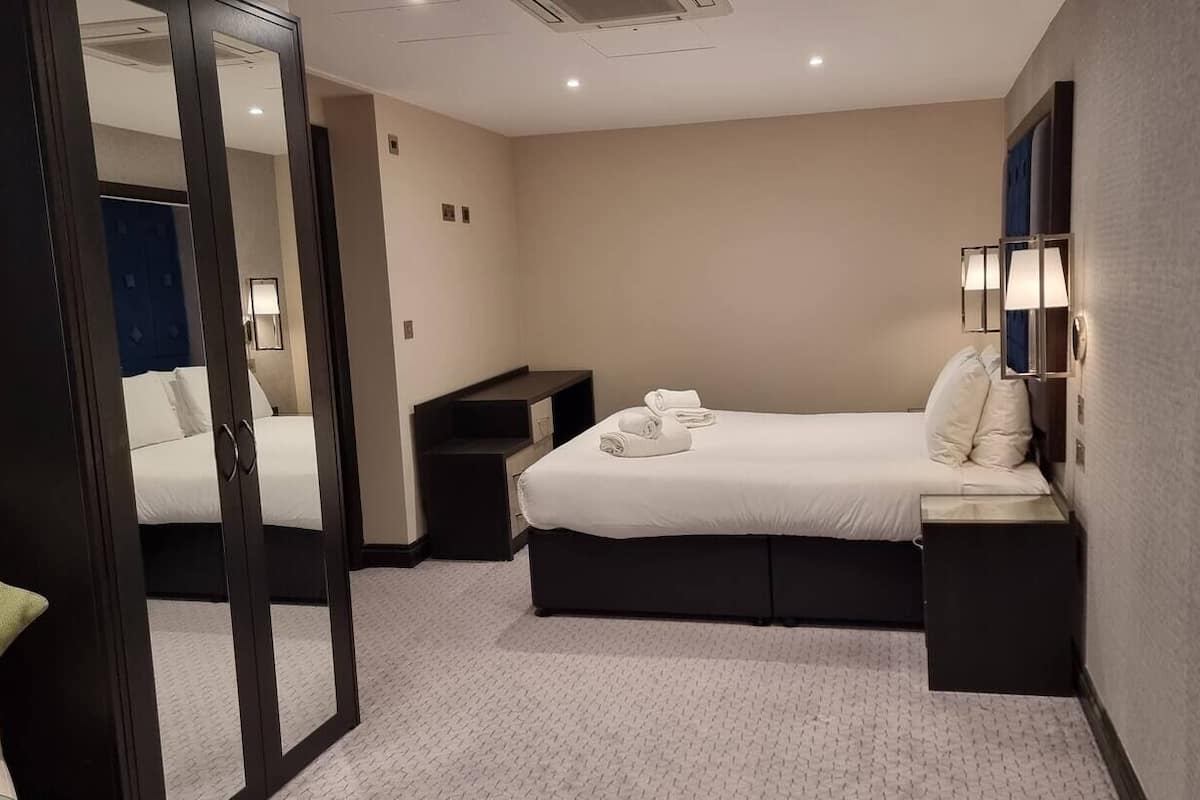 Quarto de hotel com uma cama, mesa de cabeceira e espelho.