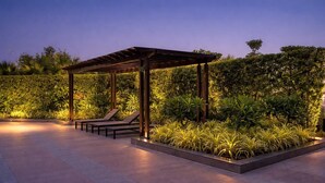 Un espacio de estar al aire libre cubierto con sillones, rodeado de vegetación cuidada y suelo empedrado.