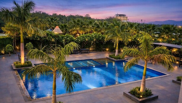 Una piscina rodeada de palmeras, un jardín ajardinado y un edificio al fondo.