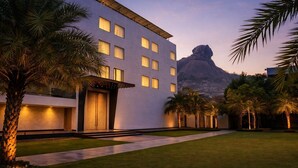 Un hotel moderno con techo plano, múltiples ventanas y un césped bien cuidado con palmeras.