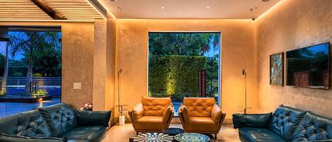 A modern lounge area with leather sofas, a large window with a view of greenery, and a patterned coffee table.