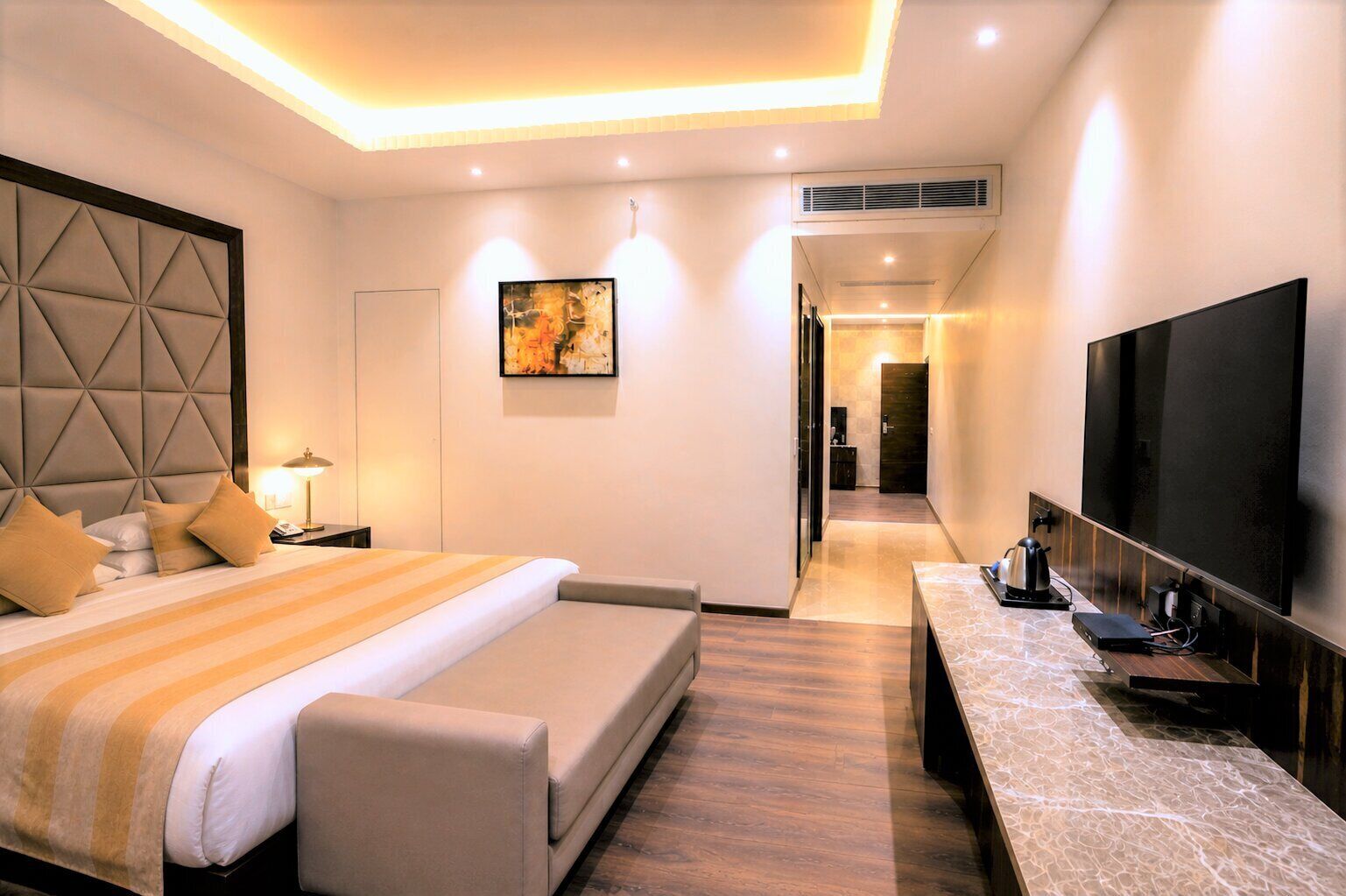 Une chambre d’hôtel moderne dotée d’un grand lit, d’un téléviseur à écran plat, d’un bureau avec une machine à café et d’un tableau au mur.