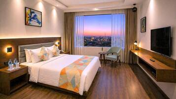 A hotel room with a large bed, a TV, a chair, a desk, and a window with a city view.
