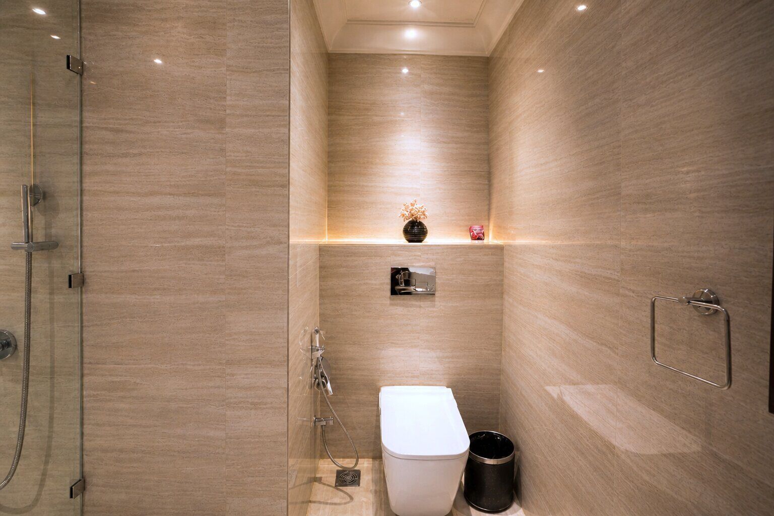 A modern bathroom with a glass shower enclosure, a toilet, and a trash bin.