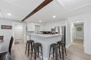 Une cuisine moderne avec des meubles blancs, un îlot central doté de tabourets et un coin repas avec une table et des chaises.