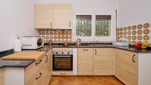 Een kleine keuken met houten kastjes, een ingebouwde oven, een magnetron en een raam met uitzicht op bomen.