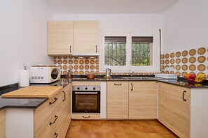 A compact kitchen with wooden cabinets, a built-in oven, a microwave, and a window with a view of trees. - 1MASS 01 - House divided into two independent apartments only 200m from Llafranc beach (Llafranc)