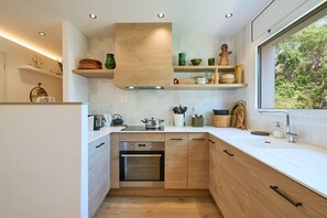 A modern kitchen with wooden cabinets, a built-in oven, and a window providing a view of greenery. - 1XER01 - Cozy renovated apartment for 6 people in Calella de Palafrugell (Calella de Palafrugell)